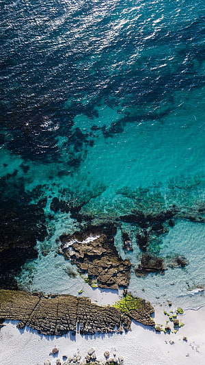 Aerial View of Turquoise Ocean Water Lapping Against Rocky Shoreline and White Sand Beach HD phone wallpaper