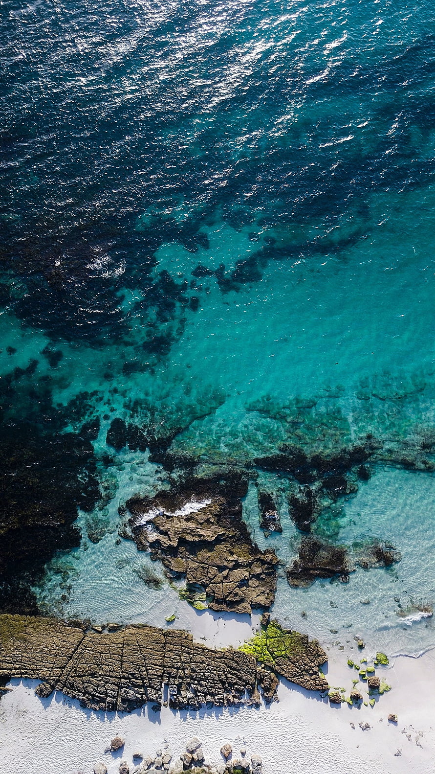 Aerial View of Turquoise Ocean Water Lapping Against Rocky Shoreline and White Sand Beach HD phone wallpaper
