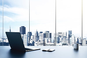 Modern Office Desk with Laptop and Notebook Overlooking City Skyline Through Floor-to-Ceiling Windows HD wallpaper