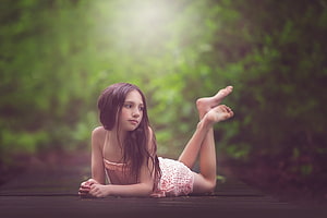 Young Girl Lying on Wooden Deck in Lush Green Forest with Soft Sunlight HD wallpaper
