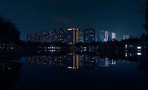 City skyline reflected in a calm lake at night with illuminated high-rise buildings HD wallpaper