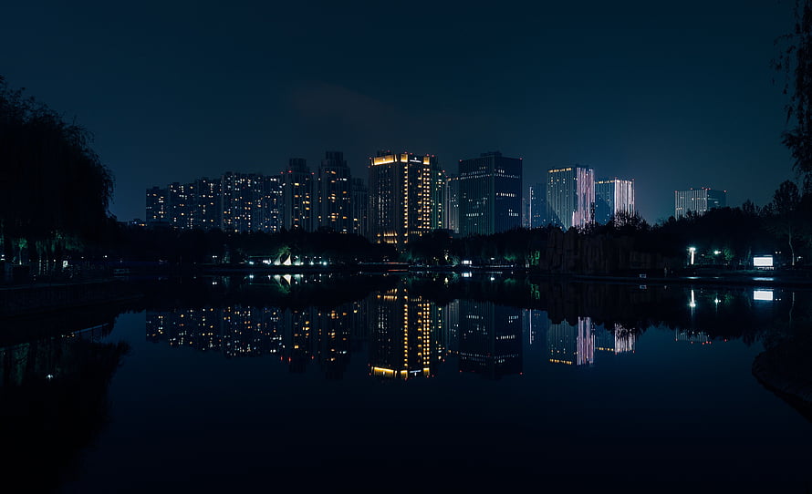City skyline reflected in a calm lake at night with illuminated high-rise buildings HD wallpaper