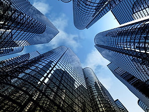 Low-angle view of modern glass skyscrapers converging against a blue sky with scattered clouds HD wallpaper
