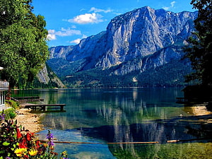 Serene Alpine Lake with Mountain Reflections, Wooden Pier, and Vibrant Shoreline Flowers HD wallpaper