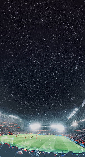 Snowfall Over a Lit Soccer Stadium at Night with Players on the Pitch HD phone wallpaper