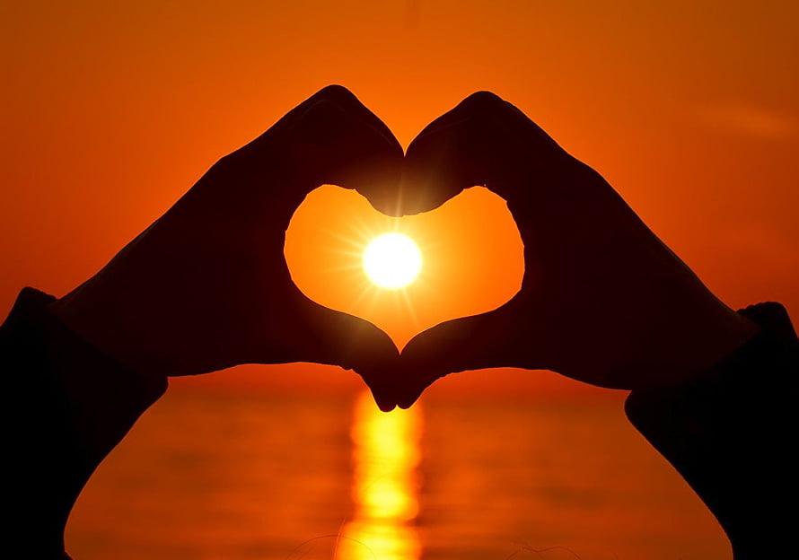 Silhouette of hands forming a heart shape framing the sun over a calm ocean at sunset HD wallpaper