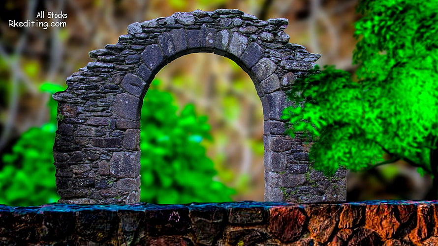 Weathered Stone Arch Ruin Framing Vibrant Green Foliage in a Lush Garden Setting HD wallpaper