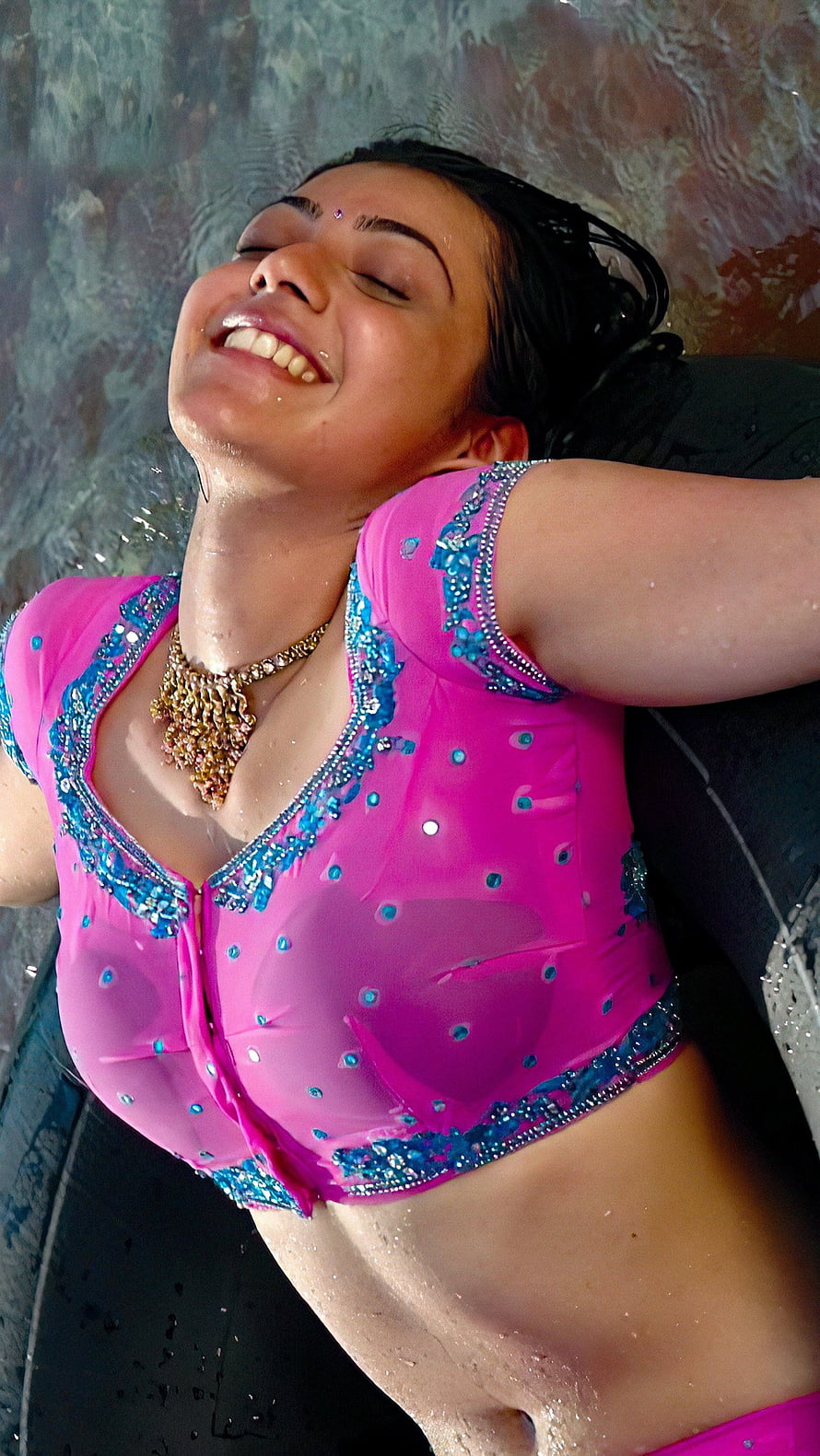 Kajal Agarwal in a vibrant pink embellished crop top with a gold necklace, smiling with eyes closed HD phone wallpaper