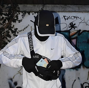 Streetwear Portrait of a Figure in White Nike Jacket and Black Supreme Sling Bag Against Graffiti Wall HD wallpaper