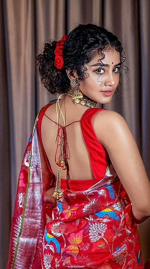 Anupama Parmeshwaran in a vibrant red embroidered saree with traditional gold jewelry and floral hair accessory HD phone wallpaper