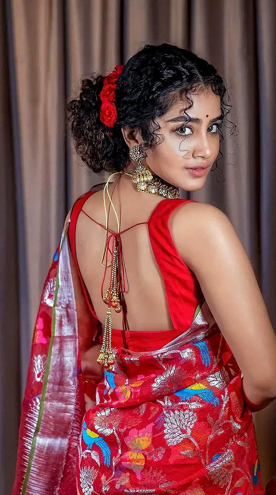 Anupama Parmeshwaran in a vibrant red embroidered saree with traditional gold jewelry and floral hair accessory HD phone wallpaper