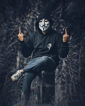 Person in black hoodie wearing a Guy Fawkes mask sitting on a stone pillar in a dark forest HD phone wallpaper