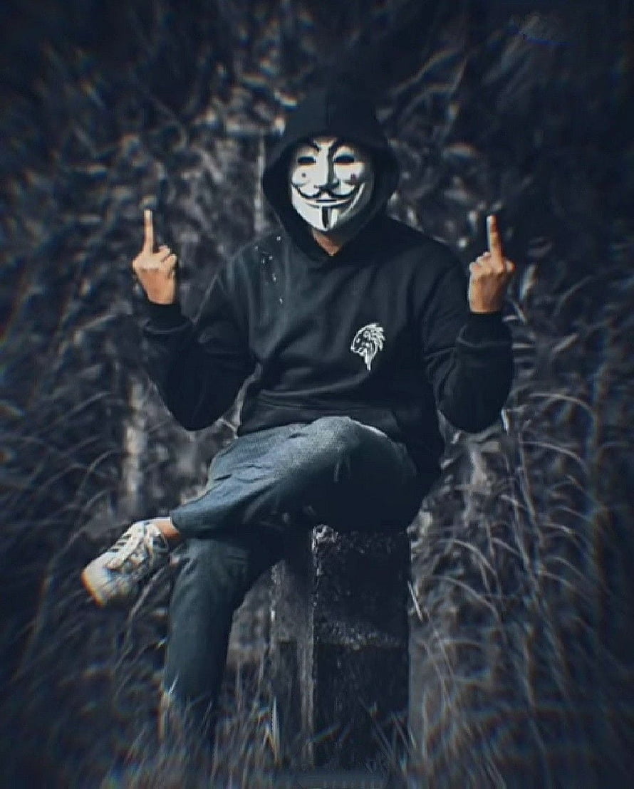 Person in black hoodie wearing a Guy Fawkes mask sitting on a stone pillar in a dark forest HD phone wallpaper
