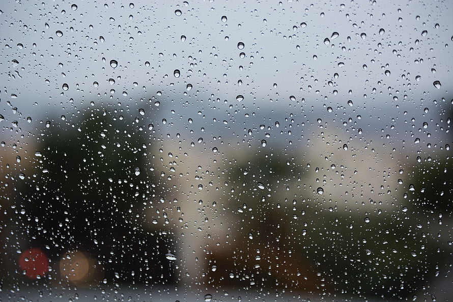 Raindrops on a glass window with a blurred cityscape and overcast sky in the background HD wallpaper