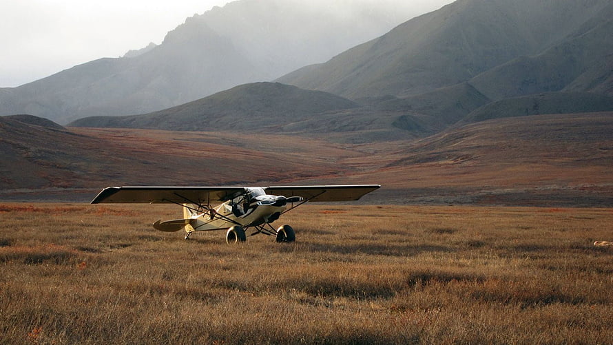 Super Cub bush plane parked in a remote mountain valley with rugged terrain backdrop HD wallpaper