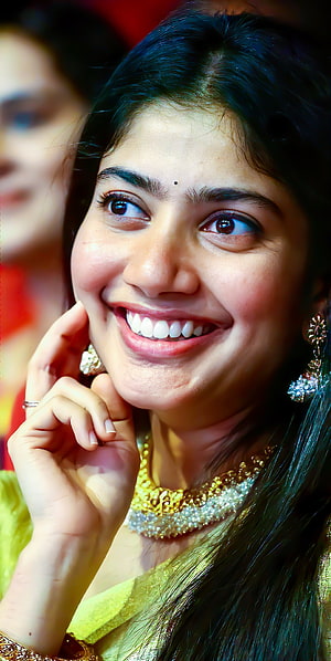 Sai Pallavi in a vibrant yellow saree with ornate gold jewelry and a warm smile HD phone wallpaper