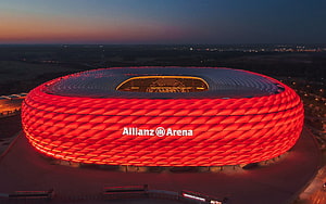 Allianz Arena in Munich glowing red at dusk with panoramic city view HD wallpaper