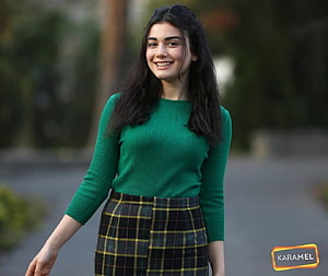 Özge Yağız in a green ribbed sweater and plaid skirt with a warm smile outdoors HD wallpaper