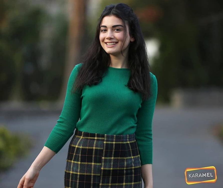 Özge Yağız in a green ribbed sweater and plaid skirt with a warm smile outdoors HD wallpaper