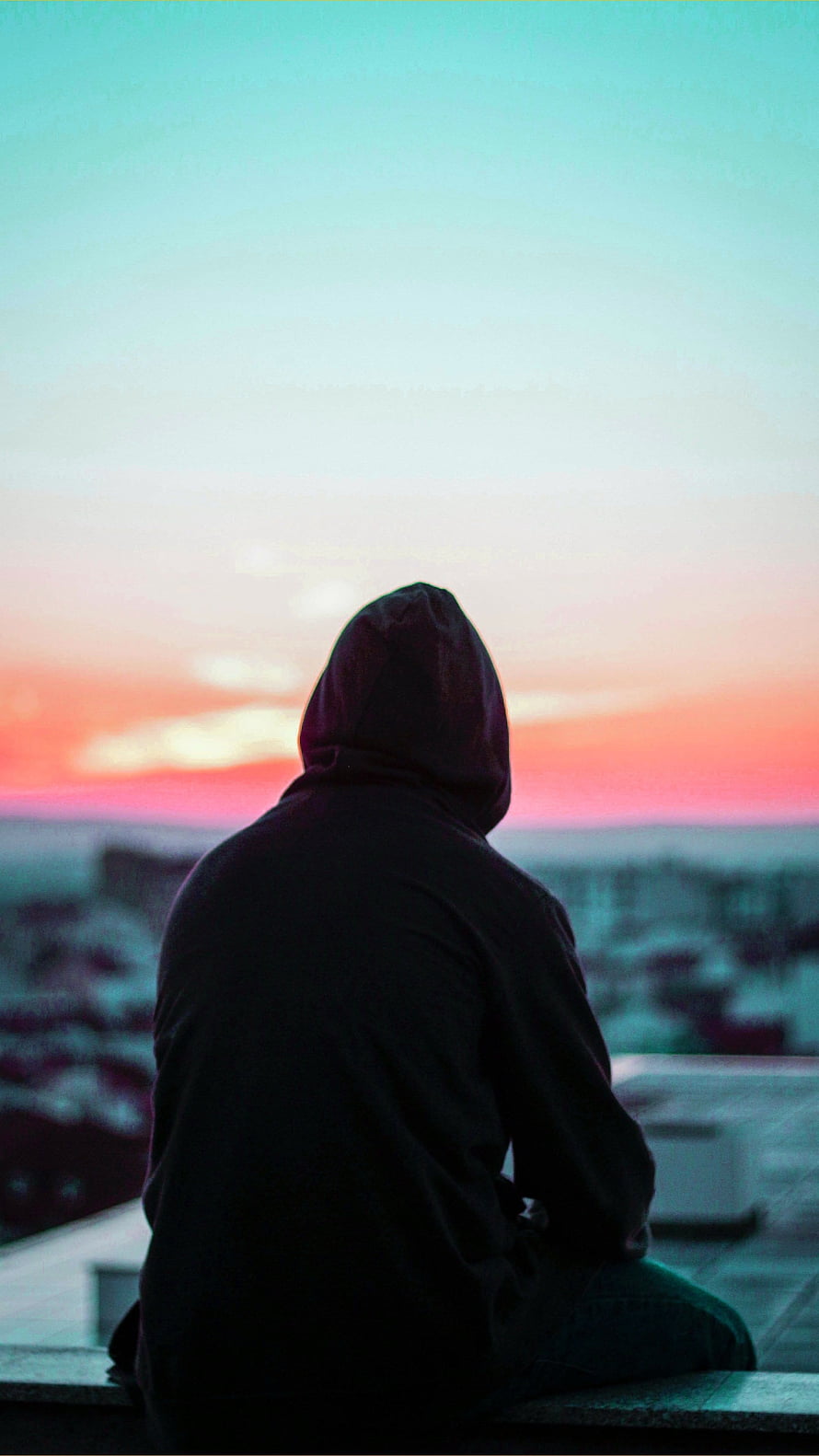Silhouette of a person in a hoodie sitting on a rooftop watching a colorful sunset over a city skyline HD phone wallpaper