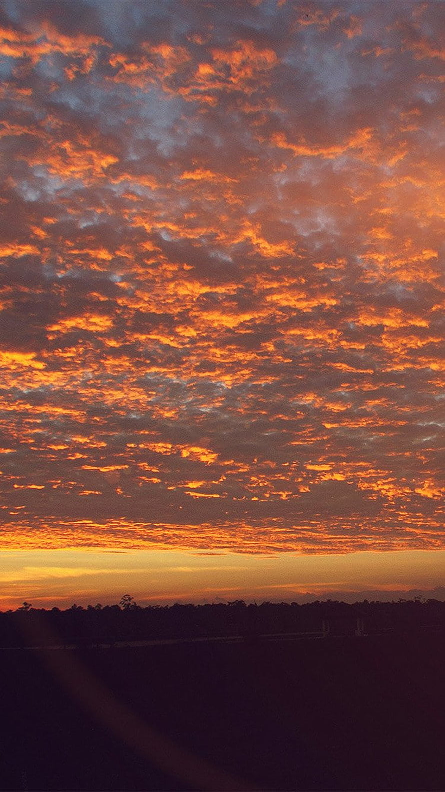 Vibrant Orange Sunset Sky with Dramatic Clouds Over a Dark Horizon HD phone wallpaper