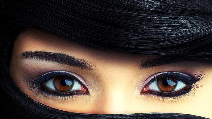 Close-up of expressive brown eyes framed by dark hair and a black hijab HD wallpaper