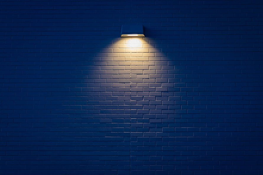 Illuminated Blue Brick Wall with Warm Sconce Light at Night HD wallpaper