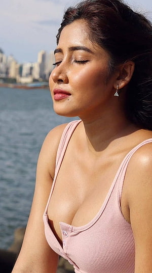 Sofia Ansari in a pink ribbed top with eyes closed against a waterfront city skyline HD phone wallpaper