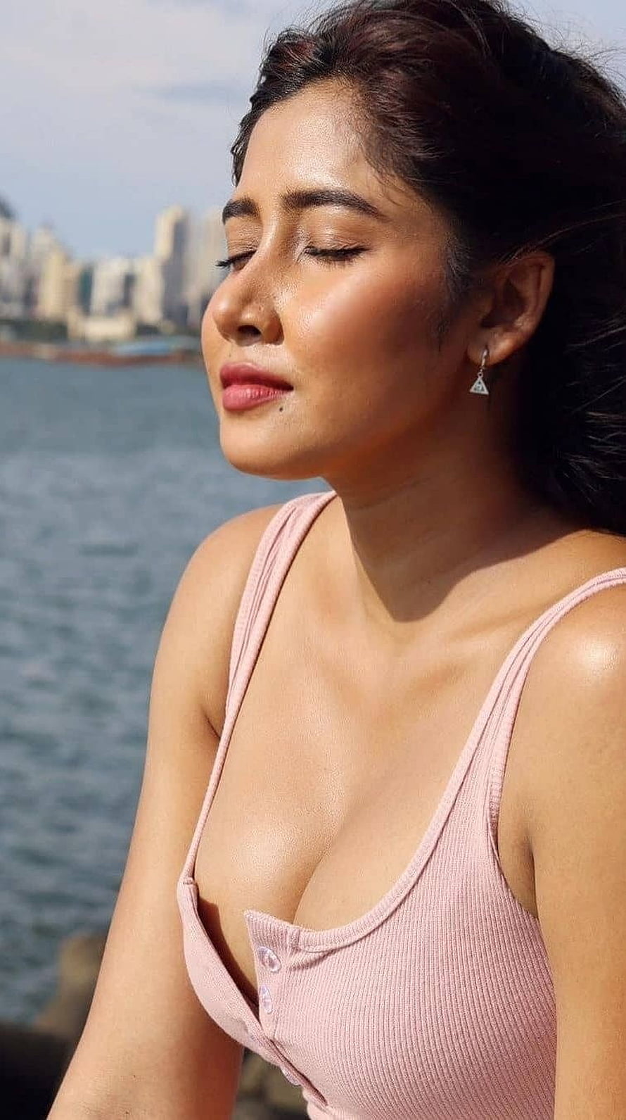 Sofia Ansari in a pink ribbed top with eyes closed against a waterfront city skyline HD phone wallpaper