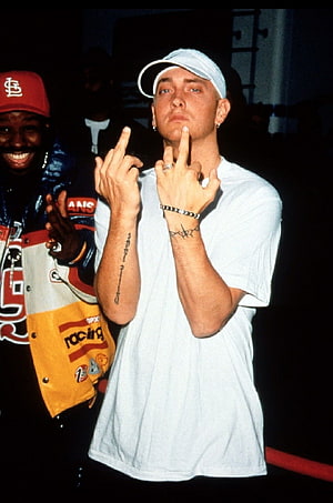 Eminem performing live on stage in a white t-shirt and cap with middle finger gesture HD phone wallpaper