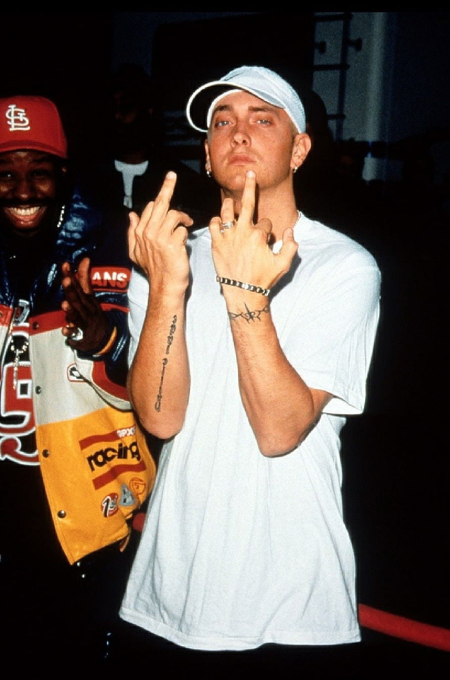 Eminem performing live on stage in a white t-shirt and cap with middle finger gesture HD phone wallpaper