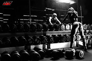 Black and white fitness model selecting dumbbells in a dark gym with mirror reflection HD wallpaper