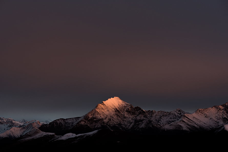 Alpine Mountain Peak Bathed in Golden Sunset Light Against a Dark Cloudy Sky HD wallpaper