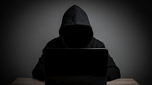 Silhouette of a hooded figure working on a laptop in a dark room HD wallpaper