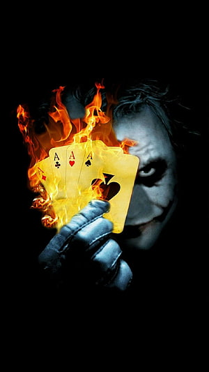 Joker holding burning aces of all suits in dramatic dark portrait HD phone wallpaper