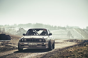 Classic BMW E30 Drift Car on a Gravel Track in a Hazy Rural Landscape HD wallpaper