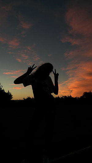 Silhouette of a person making peace signs against a vibrant orange and blue sunset sky HD phone wallpaper