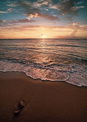 Golden sunset over calm ocean waves lapping onto a sandy tropical beach shoreline HD phone wallpaper