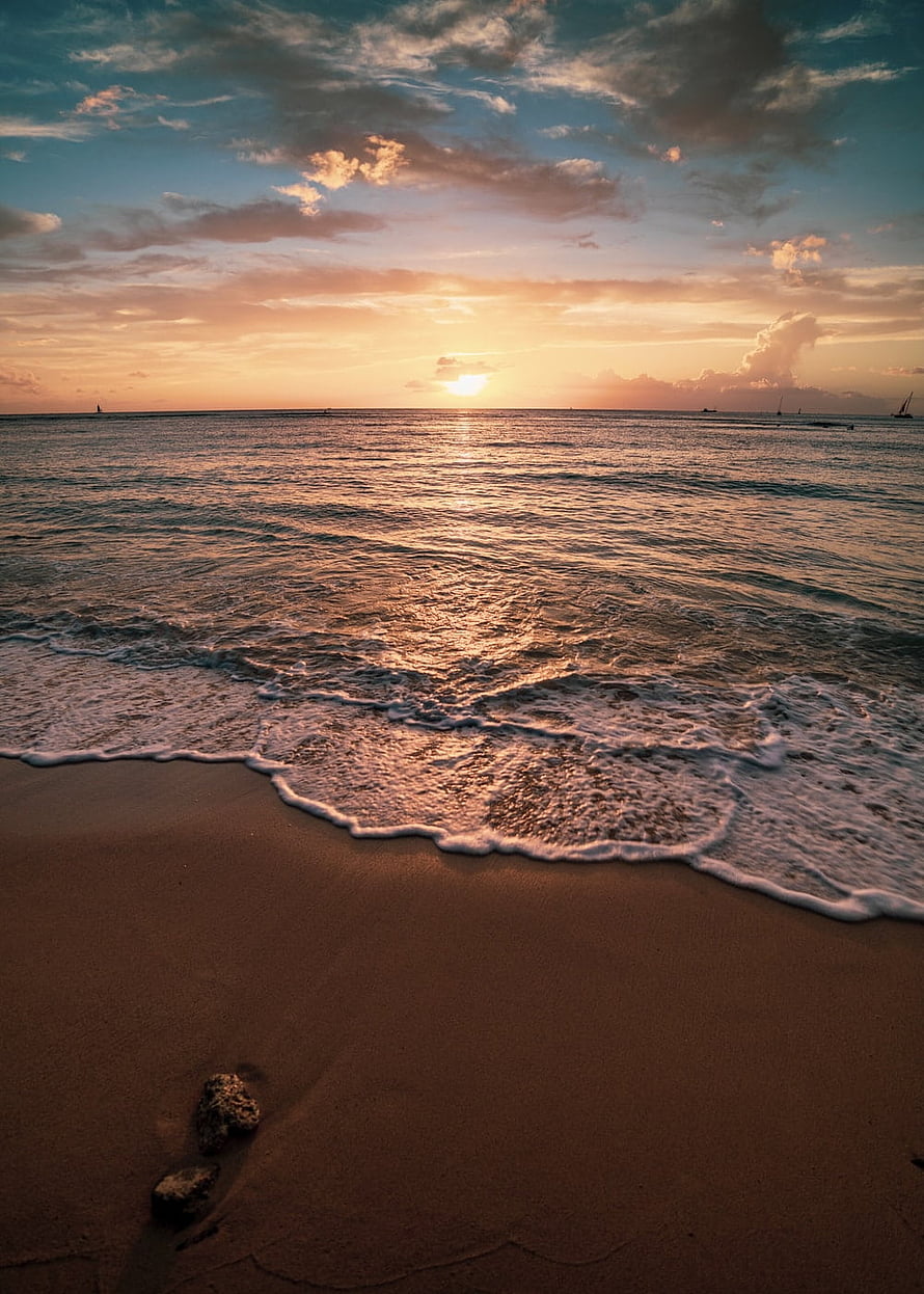 Golden sunset over calm ocean waves lapping onto a sandy tropical beach shoreline HD phone wallpaper