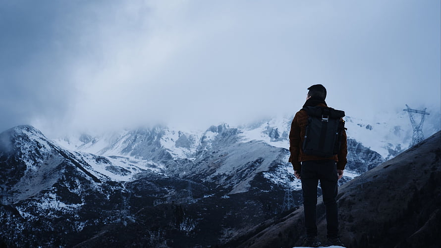 Lone Hiker with Backpack Standing on Snowy Mountain Ridge Under Overcast Sky HD wallpaper
