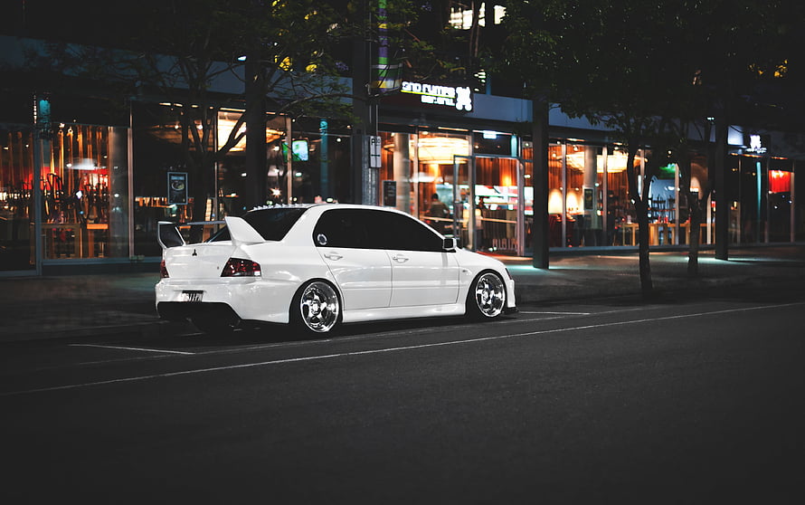 White Mitsubishi Lancer Evolution IX parked on a city street at night with illuminated storefronts HD wallpaper