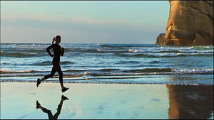 Woman Running on Wet Sand at the Beach with Rock Formation and Ocean Waves HD wallpaper