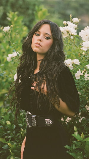 Jenna Ortega in Black Dress with Ornate Belt Amid White Garden Blooms HD phone wallpaper
