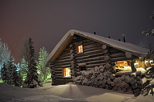 Cozy Log Cabin in Snowy Winter Night with Warm Glowing Windows and Stacked Firewood HD wallpaper