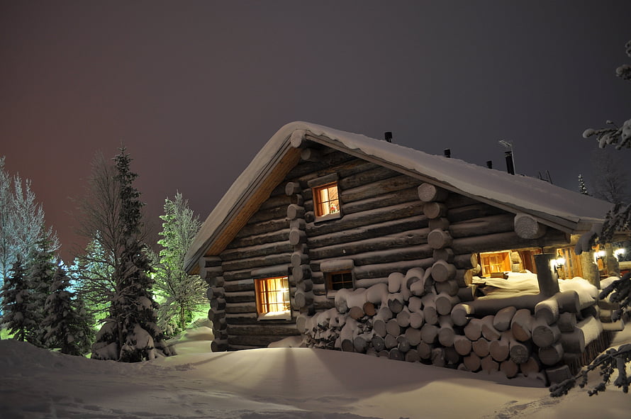 Cozy Log Cabin in Snowy Winter Night with Warm Glowing Windows and Stacked Firewood HD wallpaper