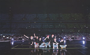 BTS Members Posing on Stage During a Concert with a Sea of Light Sticks in the Background HD wallpaper
