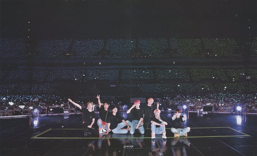 BTS Members Posing on Stage During a Concert with a Sea of Light Sticks in the Background HD wallpaper