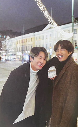BTS V and Jungkook smiling together in a European city at night with festive lights HD phone wallpaper