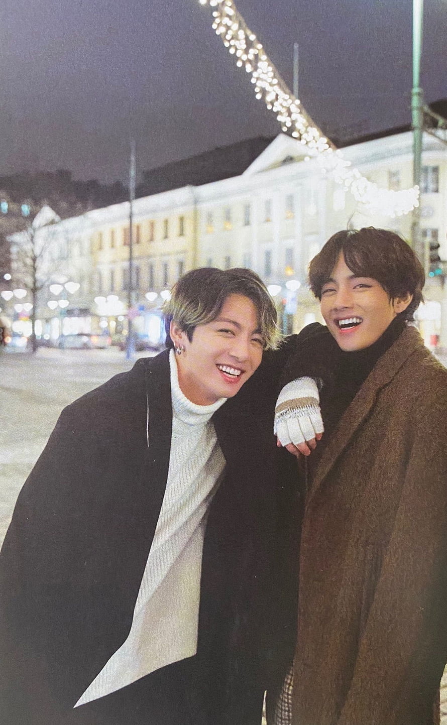 BTS V and Jungkook smiling together in a European city at night with festive lights HD phone wallpaper