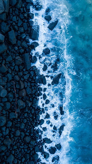 Aerial View of Turquoise Ocean Waves Crashing on Dark Rocky Shoreline HD phone wallpaper